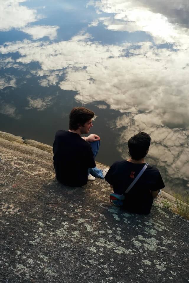 Friends sitting on a ledge with a reflection on the river