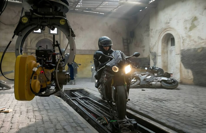 Rebecca Ferguson is on a motorbike that is on a moving platform on the set of Mission: Impossible — Rogue Nation